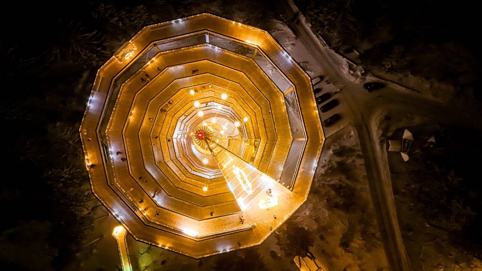 Veduta aerea notturna di una scenografica installazione luminosa a spirale in uno spazio pubblico.